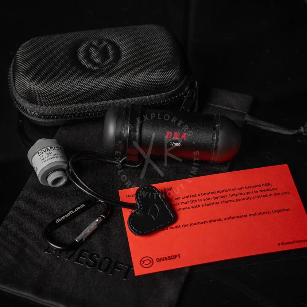 Black cylindrical divesoft dna nitrox analyzer with bluetooth, red lettering, and leather heart charm on carabiner underwater