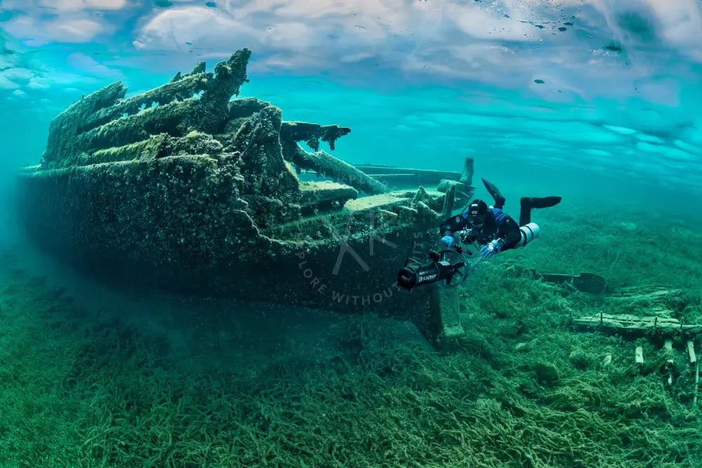 A diver in black scuba gear explores a rusted shipwreck covered in algae during the full-day kuwait islands dive trip