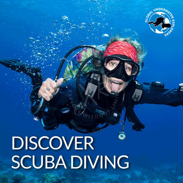A scuba diver in black gear with a red bandana and clear goggles holding up their hand underwater for gue discover diving