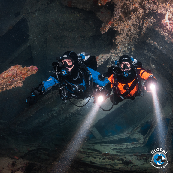 Two GUE scuba divers exploring a cave with lights, wearing GUE diving equipments configurations.