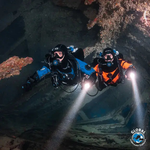 Two GUE scuba divers exploring a cave with lights, wearing GUE diving equipments configurations.
