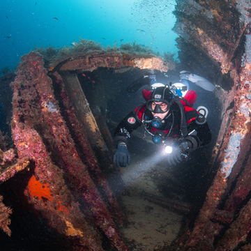 Diver exploring a sunken shipwreck with diving equipment and Student maintaining neutral buoyancy while hovering in a drysuit during class in Qatar