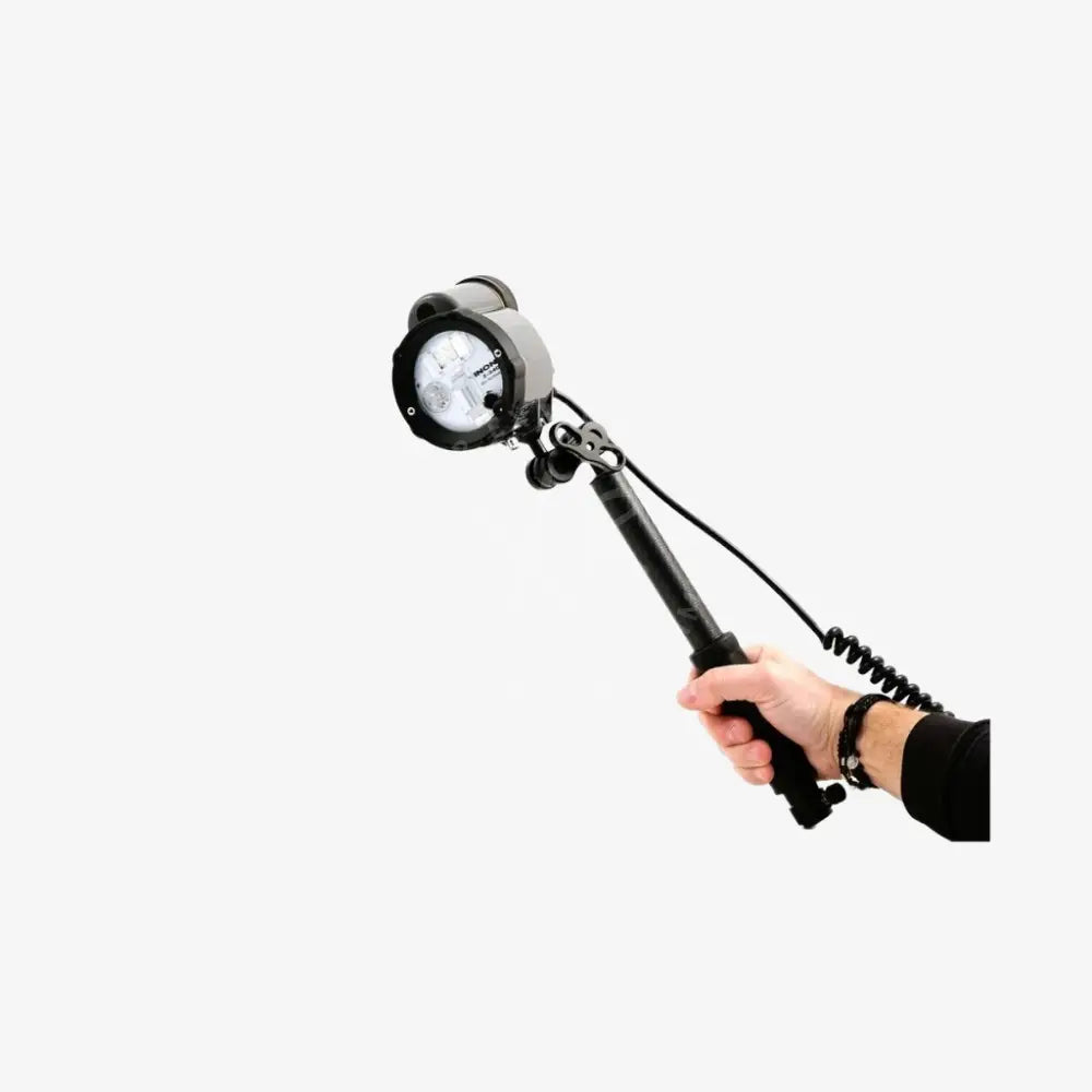 Black handheld spotlight with circular head and coiled cable attached to quick release carbon arm with grip